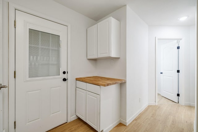 interior space featuring light wood finished floors, butcher block countertops, white cabinets, and baseboards