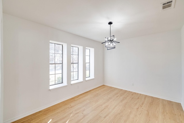 empty room featuring visible vents, baseboards, light wood-style flooring, and a chandelier