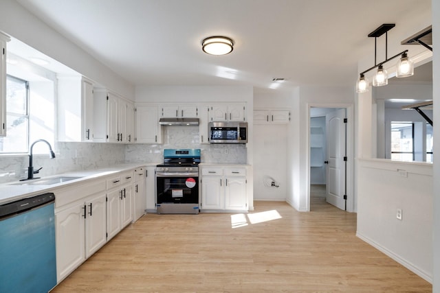 kitchen featuring a sink, under cabinet range hood, appliances with stainless steel finishes, white cabinetry, and tasteful backsplash