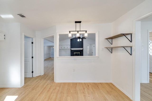 unfurnished dining area featuring visible vents, baseboards, lofted ceiling, light wood-style flooring, and a fireplace