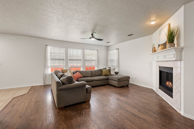 living room with dark wood finished floors, a tile fireplace, visible vents, and ceiling fan