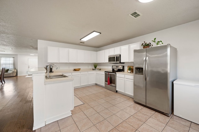 kitchen with visible vents, a sink, stainless steel appliances, white cabinets, and light countertops