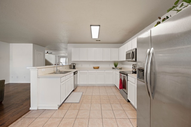 kitchen featuring a peninsula, light tile patterned flooring, a sink, white cabinets, and appliances with stainless steel finishes