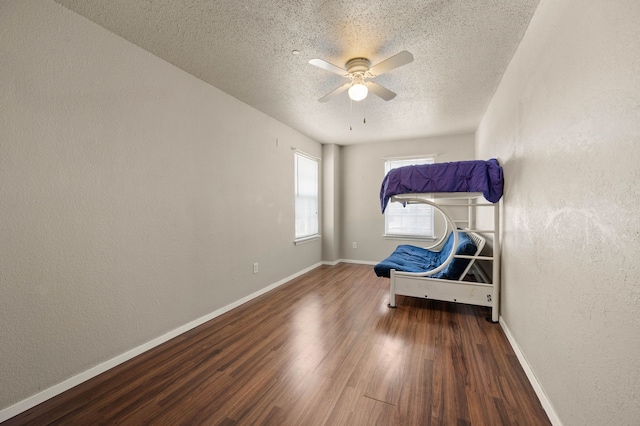 unfurnished bedroom with baseboards, a textured ceiling, wood finished floors, and a textured wall