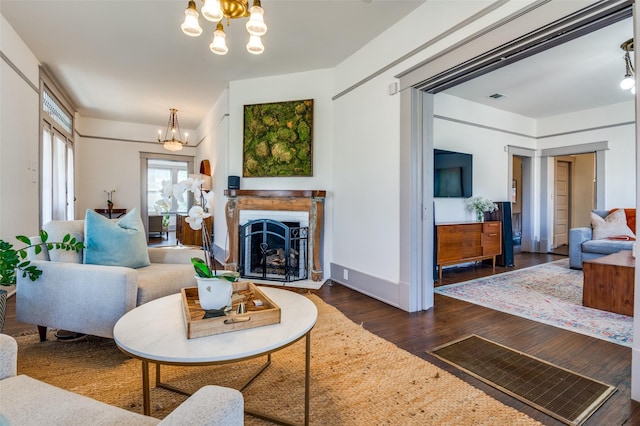 living room featuring baseboards, visible vents, an inviting chandelier, a fireplace with raised hearth, and dark wood-style flooring