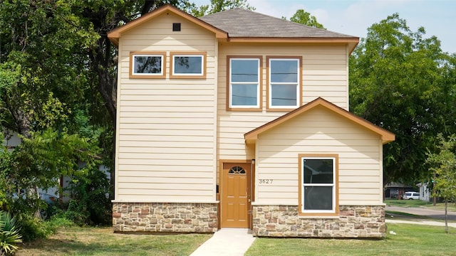 view of front facade featuring stone siding, a front lawn, and roof with shingles