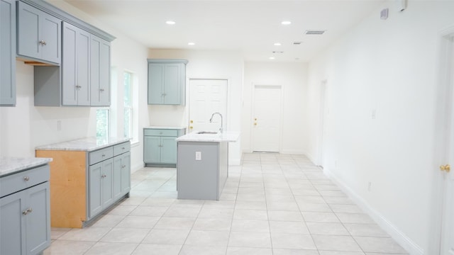 kitchen featuring visible vents, a center island with sink, a sink, recessed lighting, and light countertops