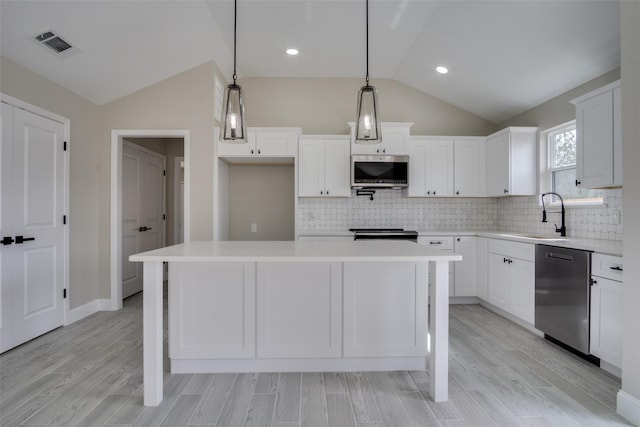 kitchen featuring visible vents, a kitchen island, vaulted ceiling, light countertops, and appliances with stainless steel finishes