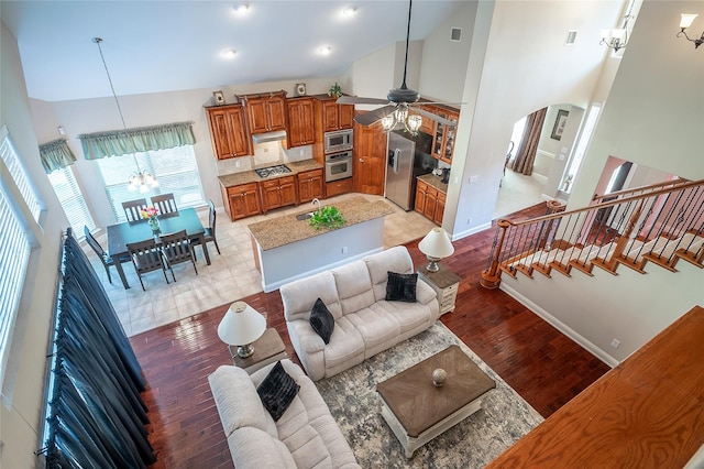 living room featuring light wood finished floors, baseboards, stairs, arched walkways, and high vaulted ceiling