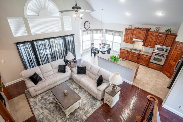 living area with a ceiling fan, baseboards, light wood finished floors, and high vaulted ceiling