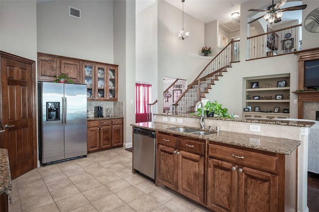 kitchen featuring visible vents, a sink, light stone counters, stainless steel appliances, and glass insert cabinets