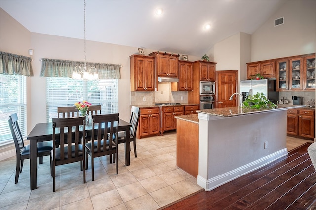 kitchen featuring under cabinet range hood, stainless steel appliances, brown cabinets, and visible vents