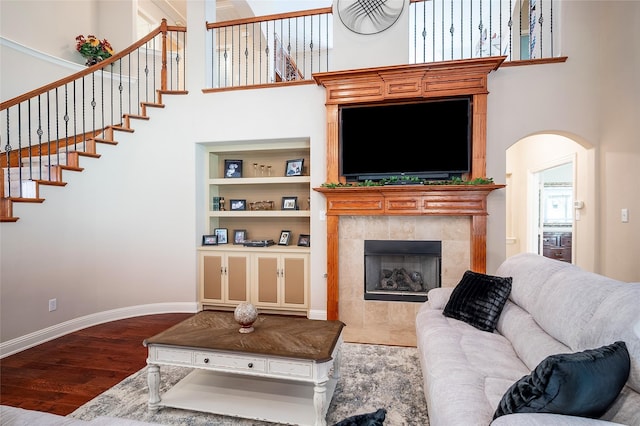 living room featuring built in features, wood finished floors, a high ceiling, a fireplace, and baseboards