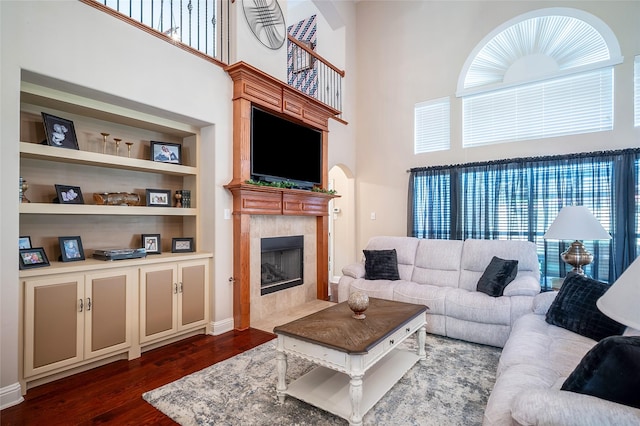 living area with a tiled fireplace, built in features, dark wood-style flooring, and a towering ceiling