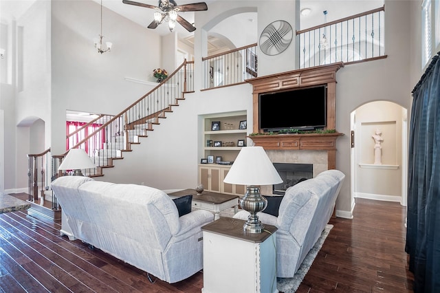 living area featuring built in shelves, dark wood-type flooring, a fireplace, baseboards, and stairs