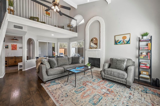 living area featuring wood finished floors, visible vents, a fireplace, arched walkways, and a towering ceiling