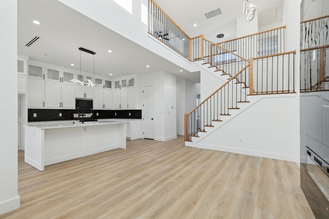 kitchen featuring visible vents, light wood-style flooring, glass insert cabinets, and a towering ceiling