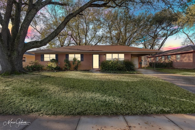 ranch-style house featuring a carport, concrete driveway, a yard, and brick siding