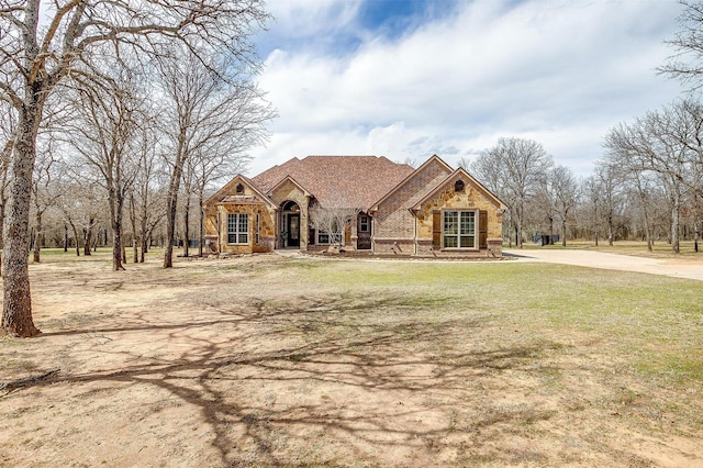 view of front of home with stone siding, brick siding, a front lawn, and a shingled roof