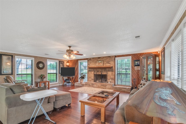 living area featuring visible vents, ornamental molding, a textured ceiling, wood finished floors, and a fireplace