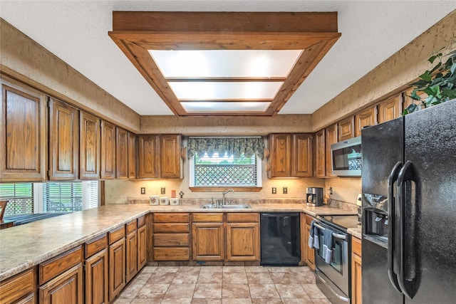 kitchen with brown cabinets, black appliances, a sink, a skylight, and light countertops