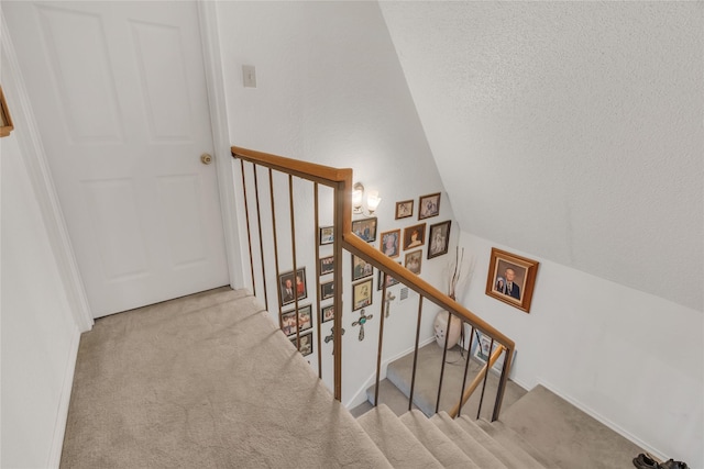 stairway featuring vaulted ceiling, carpet, and a textured ceiling