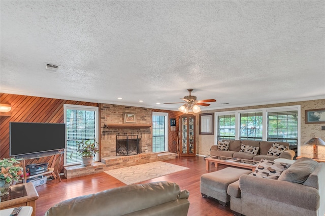 living area featuring visible vents, a brick fireplace, wood finished floors, a textured ceiling, and a ceiling fan