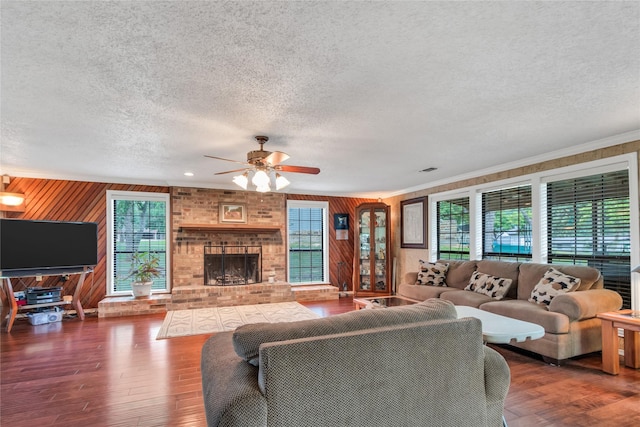 living area with a textured ceiling, wood finished floors, crown molding, a brick fireplace, and ceiling fan