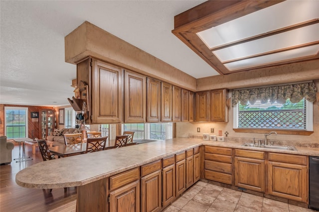 kitchen with light countertops, black dishwasher, a peninsula, brown cabinetry, and a sink