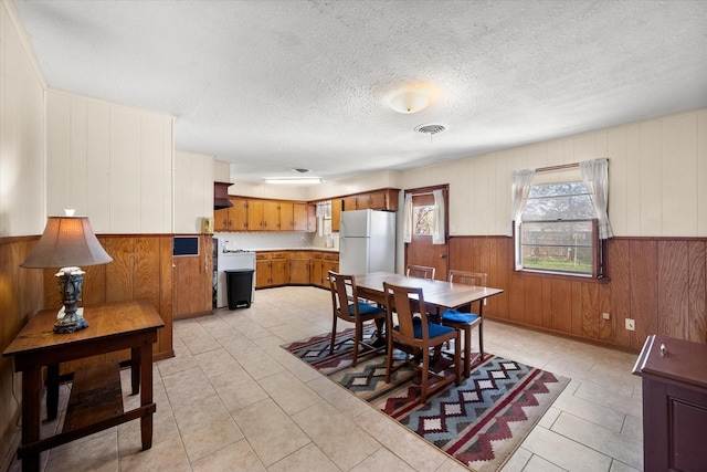 dining space with a wainscoted wall, light tile patterned flooring, visible vents, and a textured ceiling