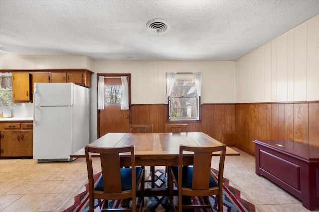 dining room with light tile patterned floors, visible vents, a textured ceiling, and a wainscoted wall