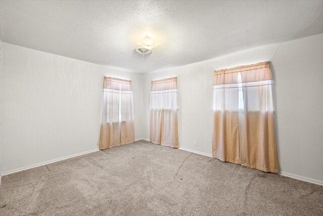 carpeted spare room featuring visible vents, baseboards, and a textured ceiling