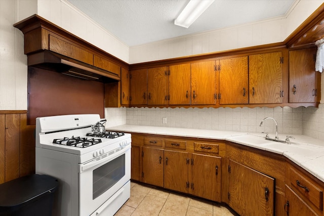 kitchen with decorative backsplash, brown cabinets, light countertops, and white range with gas stovetop