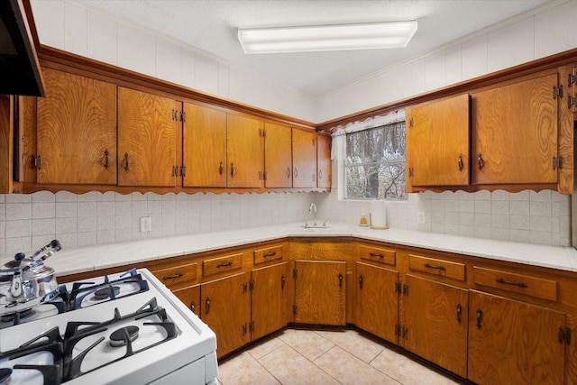 kitchen with white range with gas stovetop, brown cabinetry, and a sink