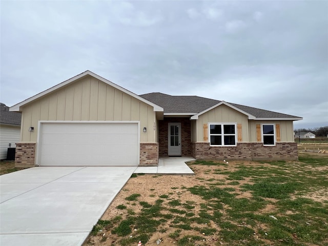 single story home featuring central air condition unit, roof with shingles, concrete driveway, a garage, and brick siding