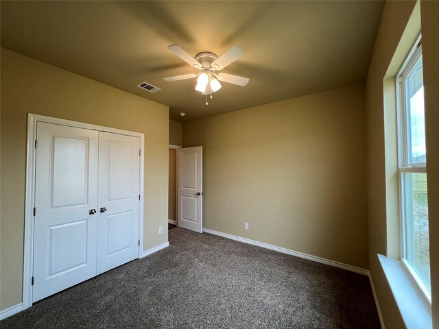 unfurnished bedroom with a ceiling fan, visible vents, baseboards, a closet, and dark carpet