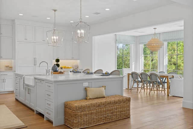 kitchen featuring backsplash, an island with sink, light wood-style flooring, white cabinets, and a sink