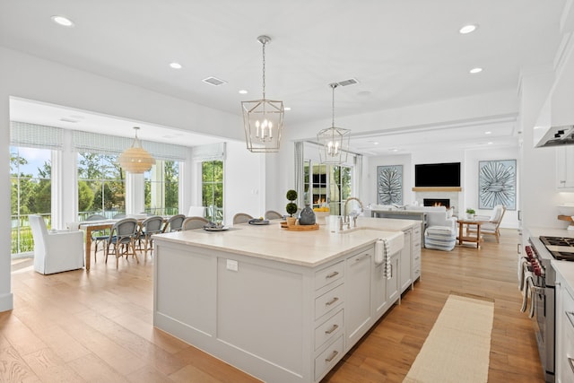 kitchen with double oven range, a warm lit fireplace, a sink, white cabinets, and light wood-type flooring