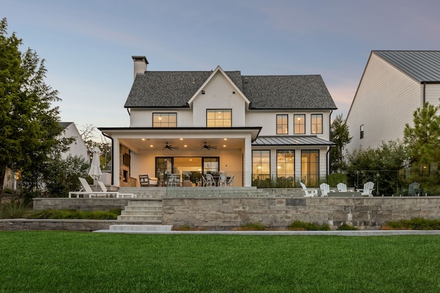 back of house at dusk featuring a lawn, a standing seam roof, a patio, metal roof, and ceiling fan