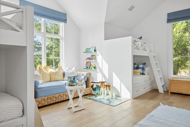 bedroom with hardwood / wood-style floors, vaulted ceiling, radiator, and multiple windows