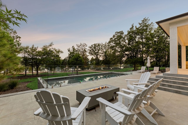 pool at dusk with a patio area, fence, a fenced in pool, and an outdoor fire pit