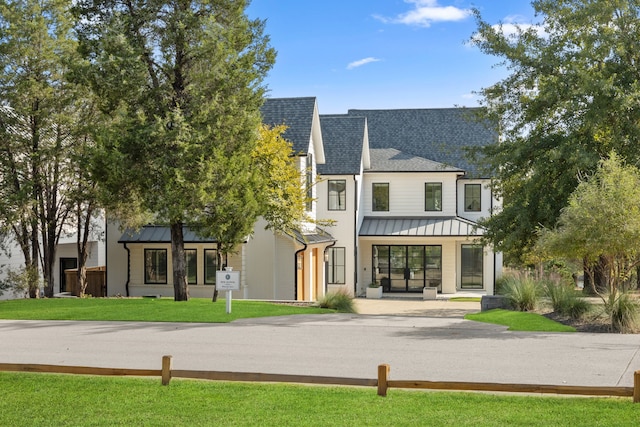 modern farmhouse style home with metal roof, roof with shingles, a front yard, and a standing seam roof