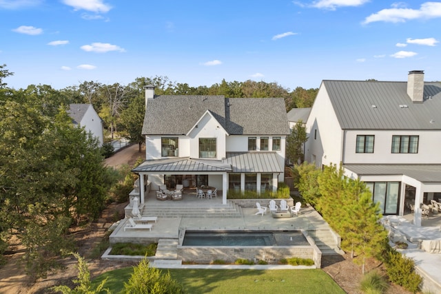 back of house featuring a chimney, outdoor dining area, metal roof, an outdoor pool, and a standing seam roof