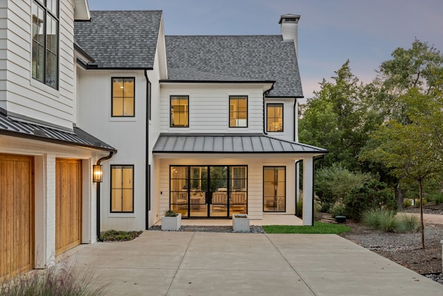 back of house with metal roof, a chimney, a standing seam roof, and a shingled roof