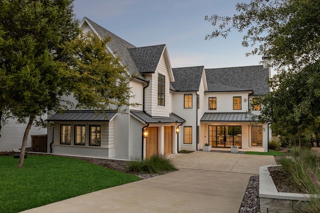 modern farmhouse style home with roof with shingles, a standing seam roof, a front lawn, concrete driveway, and a garage