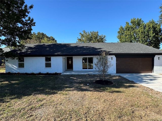 ranch-style house featuring brick siding, a shingled roof, a front yard, a garage, and driveway