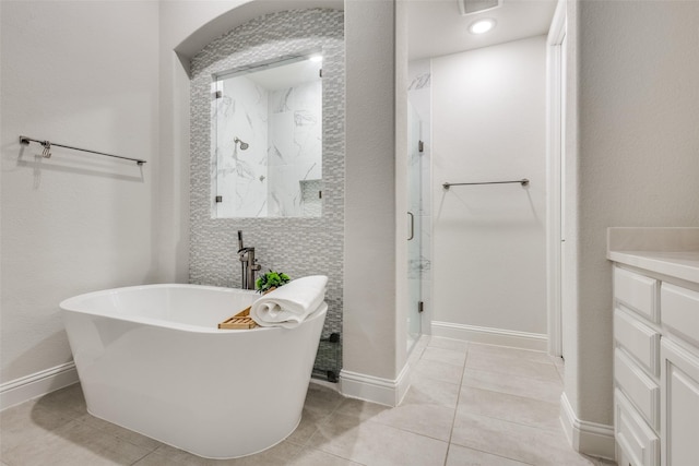 bathroom featuring a marble finish shower, tile patterned flooring, baseboards, a freestanding bath, and vanity