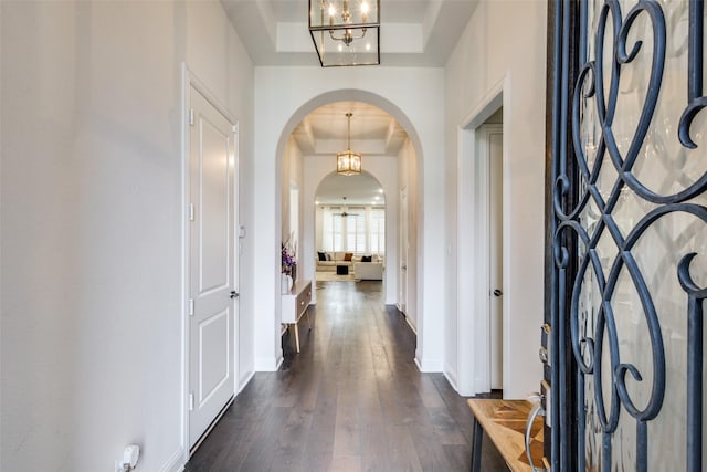 foyer featuring dark wood-type flooring, baseboards, arched walkways, and a raised ceiling