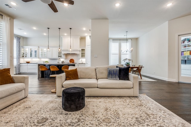 living room with dark wood finished floors, ceiling fan with notable chandelier, recessed lighting, and baseboards