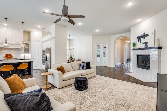 living area with recessed lighting, arched walkways, dark wood-type flooring, and a tiled fireplace